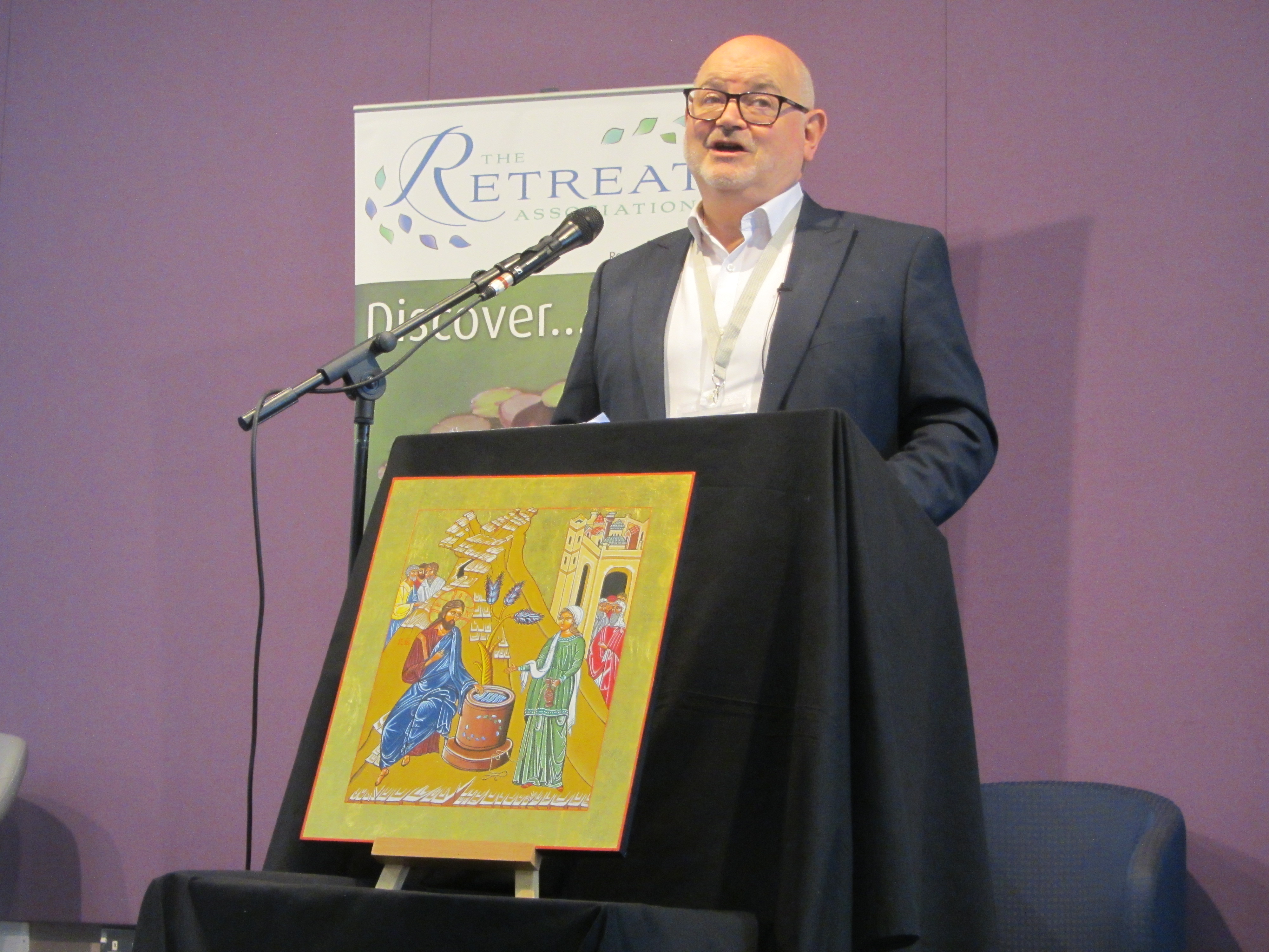 Mark Oakley speaking at an event with a purple background