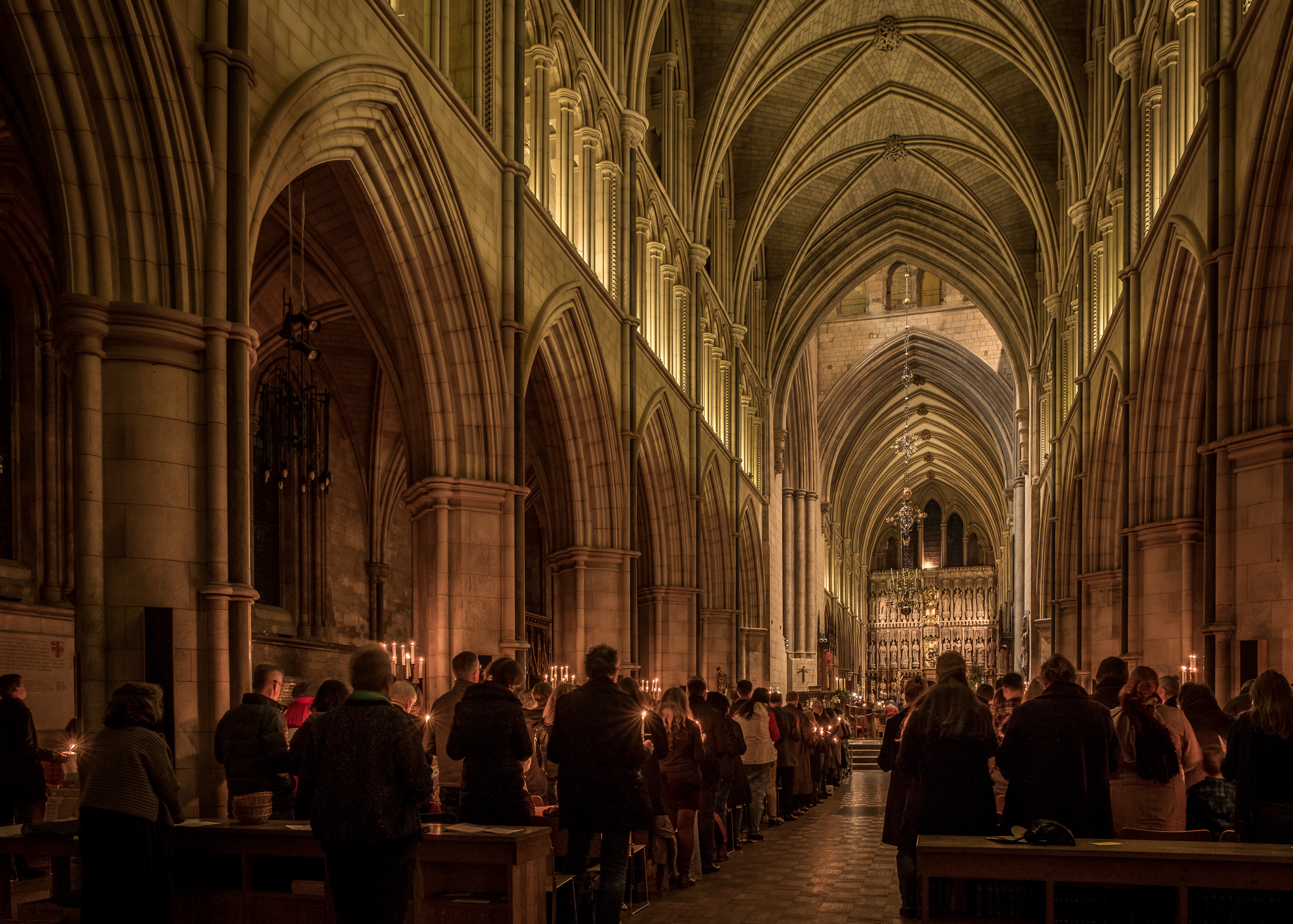 A congregation stands in the pews of a large cathedral, holding lit candles during a service.