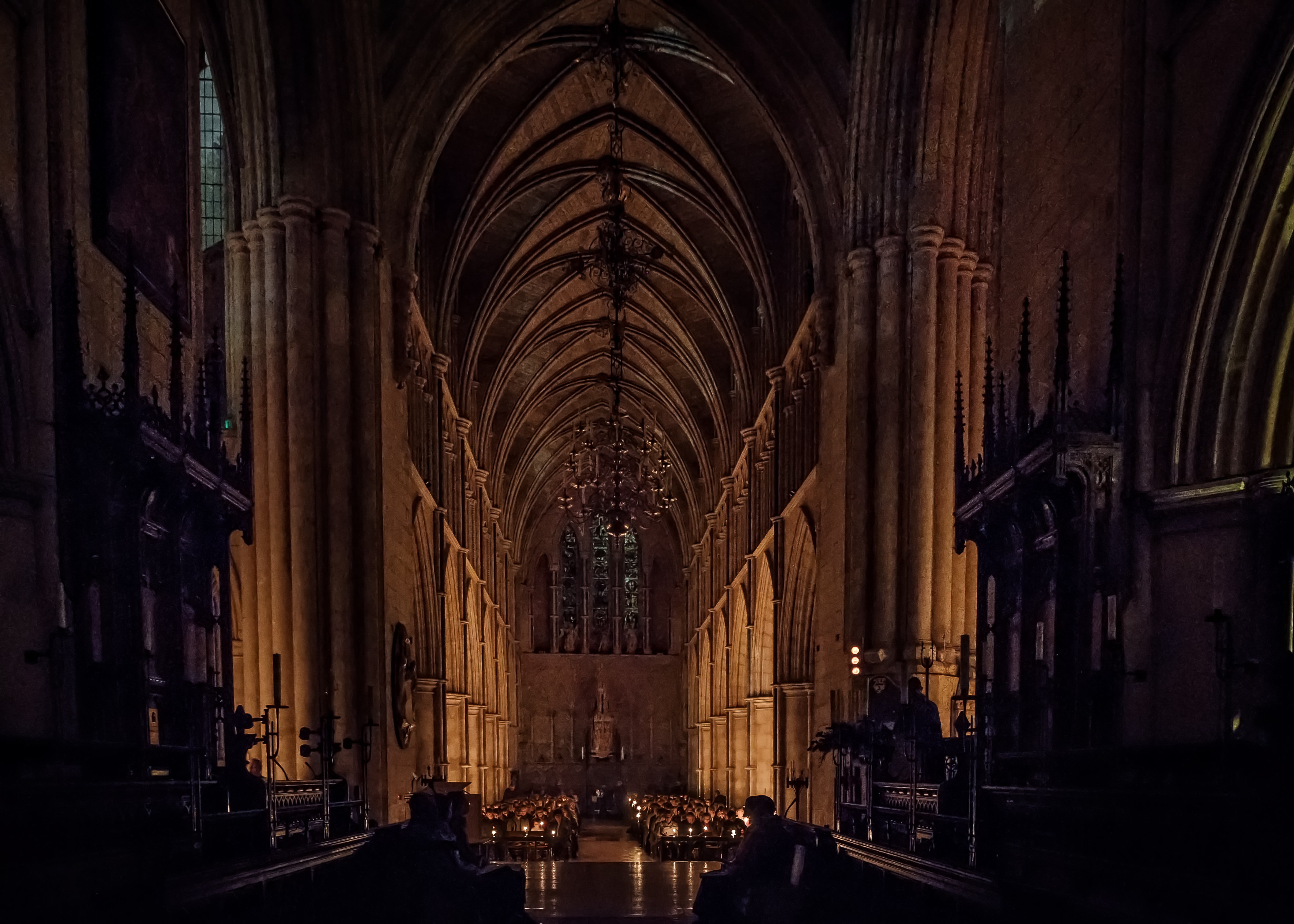 Interior view looking down the aisle of a stone cathedral toward an altar illuminated by rows of candles.